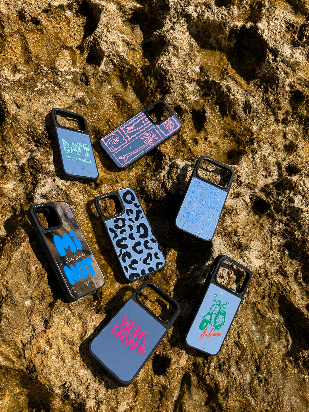 Collection de coques miroir HALLO pour iPhone photographiées sur les rochers au bord de la Méditerranée, avec des designs inspirés de Marseille, du soleil et du lifestyle du Sud