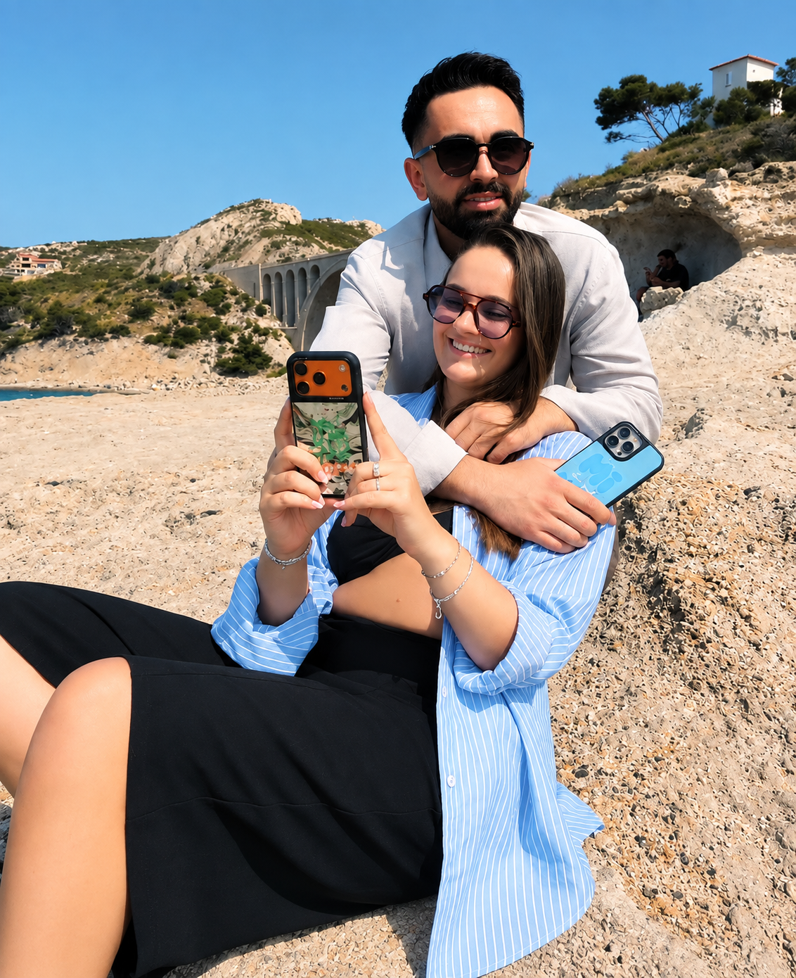 Couple utilisant des coques miroir HALLO pour iPhone sur les rochers en bord de mer à Marseille, dans une ambiance estivale inspirée du sud de la France